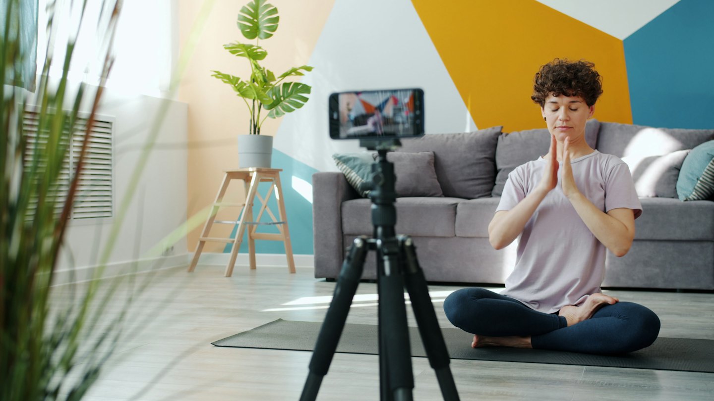 Woman meditates in a modern living room recording her session.
